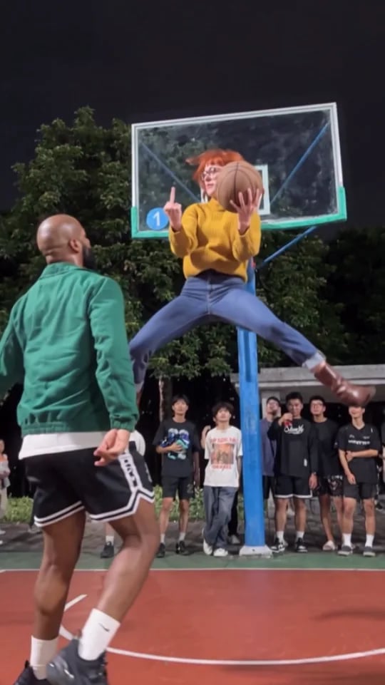 A woman with red hair in a mustard sweater leaps to the hoop with the ball as a man in a green jacket defends